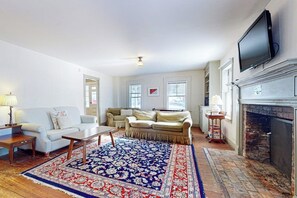 A living room with a fireplace, a television, and a patterned rug. - Convenient in-town house, river view, dog-friendly, deck, kitchen, w/d, TV, wifi (Weston)