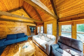 Interior de una cabaña de troncos con techo de madera, un sofá azul, un sofá blanco, un sofá marrón y una mesa de centro de madera.