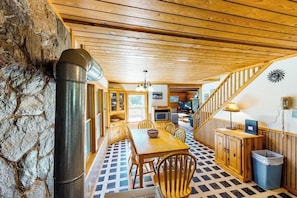 Un interior rústico con pared de piedra, techo de madera, zona de comedor con mesa y sillas, una escalera y una cocina con microondas.