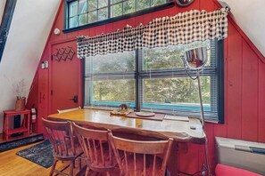 Ein rotes Interieur mit Holztisch und -stühlen, einem Fenster mit Jalousien und einem karierten Vorhang.