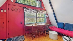 Una habitación acogedora con una puerta roja, una mesa de comedor con sillas, una ventana con persianas y un sofá rojo.