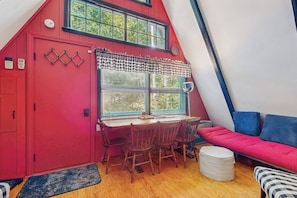 Ein gemütliches Zimmer mit roter Tür, einem Esstisch mit Stühlen, einem Fenster mit Jalousien und einem roten Sofa.