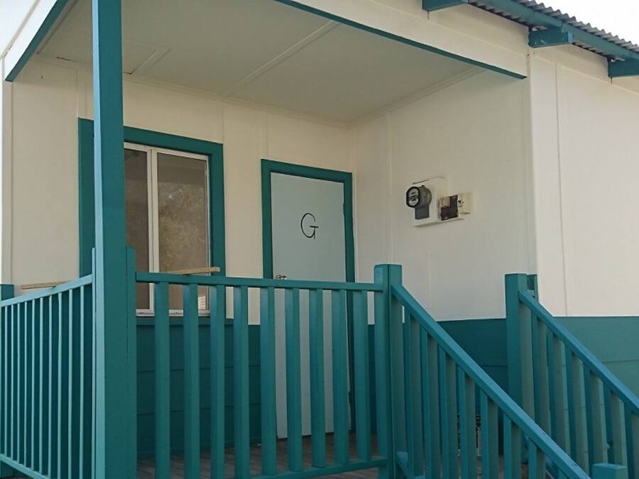 A building with a porch, a door labeled 'G', and a small wall-mounted device.