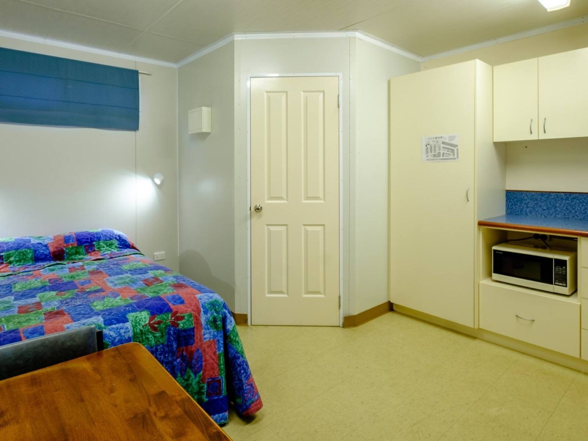 Una habitación pequeña y limpia con cama, una mesa, microondas y un armario.