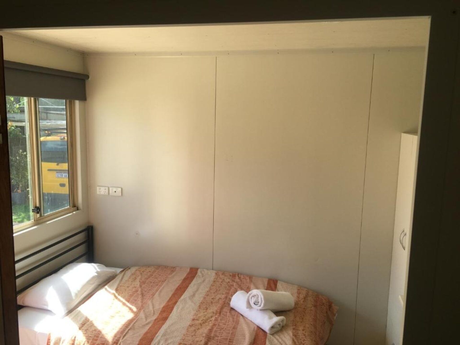 Une petite chambre avec un lit simple, une fenêtre, un radiateur et une serviette sur le lit.