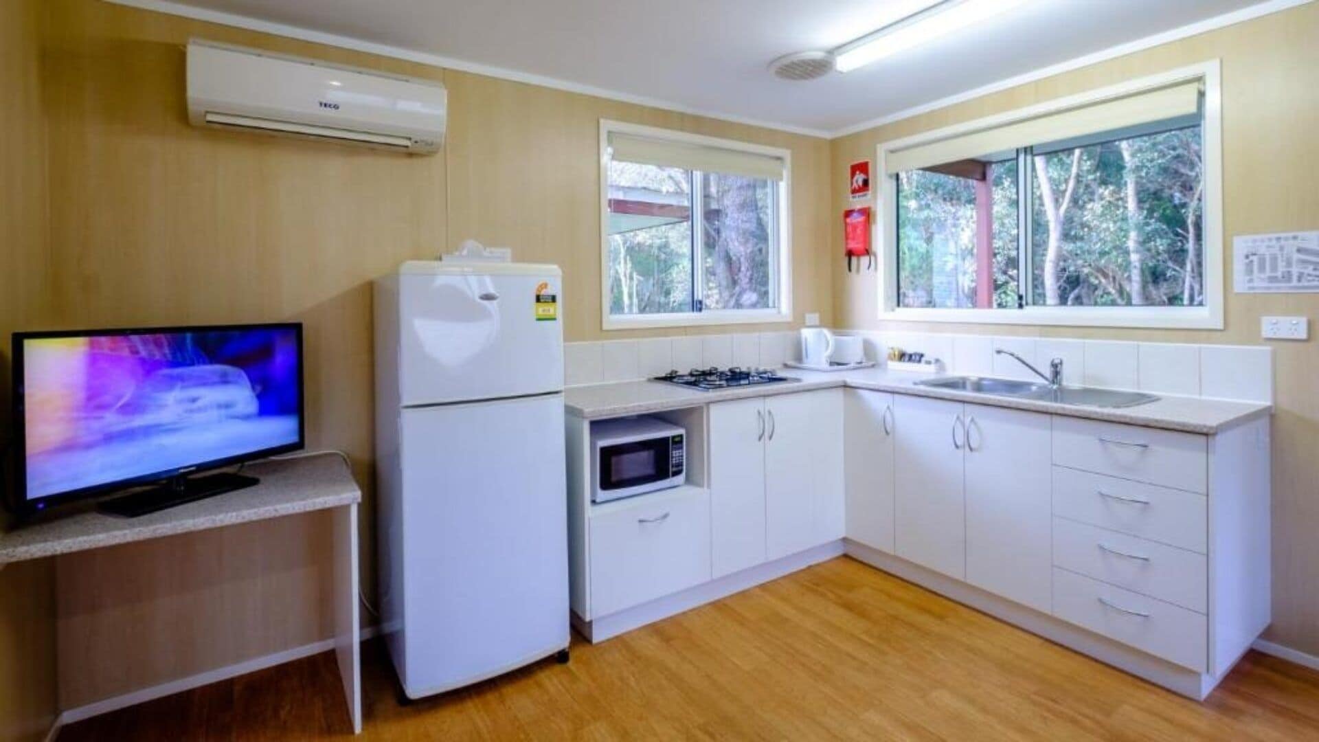 Una cocina funcional con televisor, refrigerador, microondas y pileta.
