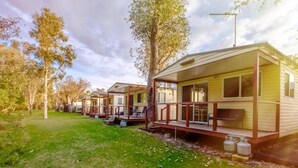A row of mobile homes with outdoor decks, surrounded by trees and grass.