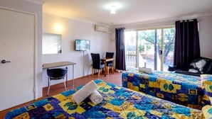 A hotel room with two beds, a desk, a chair, a TV, and a view of the outdoors.