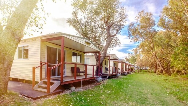 A row of mobile homes with external staircases, surrounded by trees and grass.