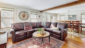 A living room with a sectional sofa, a round coffee table, and a large wall clock. - Cozy farmhouse w/ mountain views, woodstove, bbq, cable, close to Okemo, w/d (Cavendish)