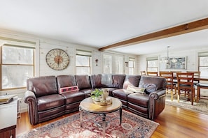 A living room with a sectional sofa, a round coffee table, and a large wall clock. - Cozy farmhouse w/ mountain views, woodstove, bbq, cable, close to Okemo, w/d (Cavendish)
