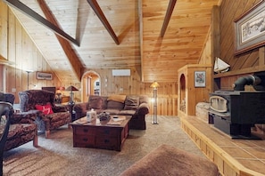 Ein gemütliches Blockhaus-Interieur mit Kamin, Holzwänden, einer Couch, einem Sessel und einem Couchtisch.