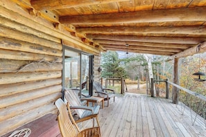 Eine Holzhütte mit einer Veranda, Holzstühlen und einer Glasdoor, die nach draußen führt.