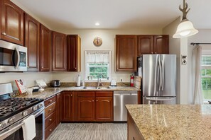 A kitchen with wooden cabinets, stainless steel appliances, a granite countertop, and a window with a view of greenery. - Winhall house on a corner lot with gas fireplace near Stratton and Bromley (Winhall)