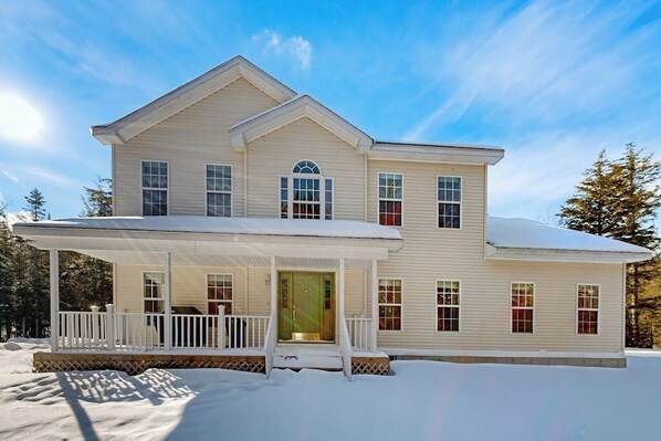 A two-story house with a covered porch, a central entrance, and a symmetrical facade. - Elegant house in quiet neighborhood, close to ski mountains, gas fireplace, wifi (Winhall)