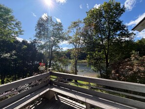 A wooden deck with a railing, overlooking a lake with trees and a clear sky.