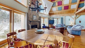 A spacious room with a large wooden dining table, comfortable seating, a fireplace, and a television. - Lakefront house w/ mountain views, waterfront, gameroom, gym, a/c, w/d (Ludlow)