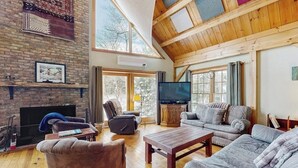 A spacious living room with a fireplace, a television, and a large window. - Lakefront house w/ mountain views, waterfront, gameroom, gym, a/c, w/d (Ludlow)