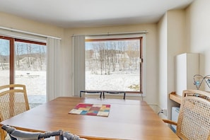 Ein Zimmer mit Holztisch, Stühlen, einem Fenster mit Vorhängen und Blick auf eine verschneite Landschaft.