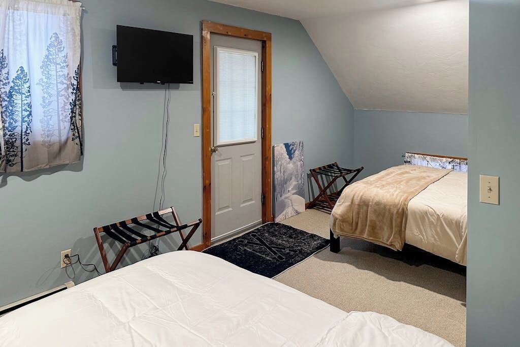 Une chambre avec deux lits, une télévision, une porte et une fenêtre avec des rideaux.