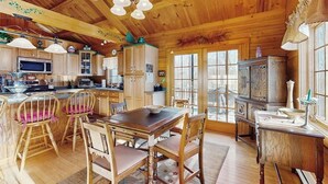 Un intérieur en bois comprenant une table à manger, des chaises, un coin cuisine et une grande fenêtre.