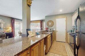 Eine Küche mit Granitarbeitsplatten, Holzschränken, einem Kühlschrank und einer Wanduhr.