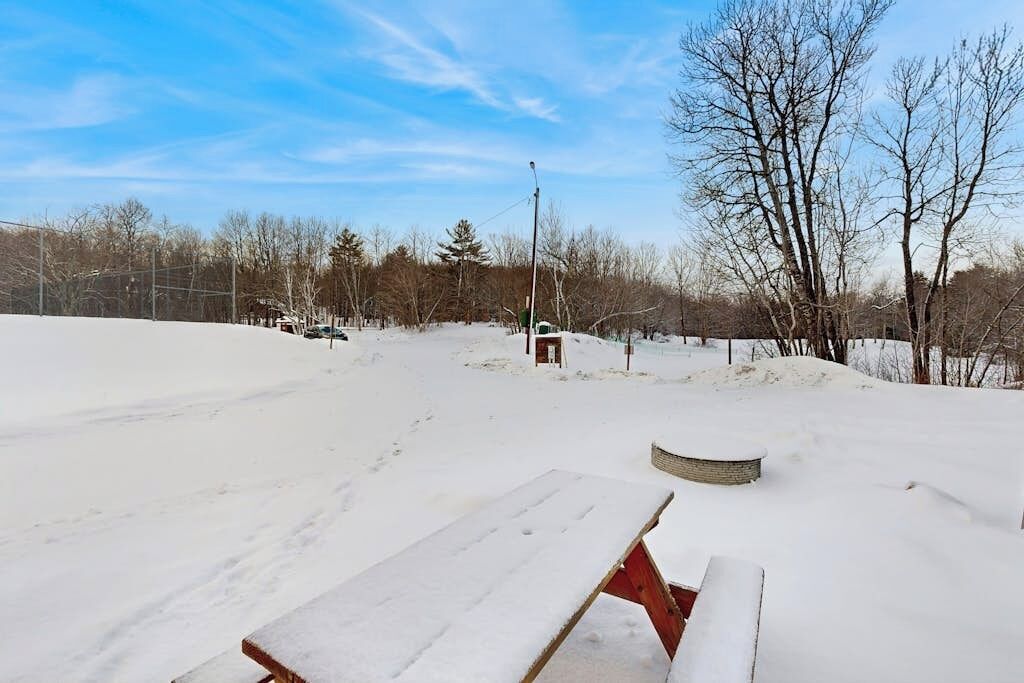 A snow-covered outdoor area with a picnic table and a small brick structure.