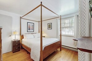 Ein Bett mit Himmelbettgestell aus Holz, ein Nachttisch mit Lampe und ein Fenster mit Vorhängen.