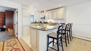 Una cocina con armarios blancos, una isla central con taburetes de bar y un microondas sobre la isla.