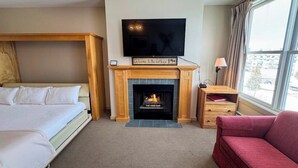 A hotel room with a bed, a fireplace, a television, a window with curtains, and a red sofa. - Walk to lifts, condo at Stratton Mountain, fireplace, pool, hot tubs, sauna (Stratton)