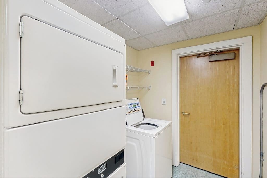 Une buanderie avec des machines à laver et des sèche-linge superposés, une porte en bois et un luminaire au plafond.