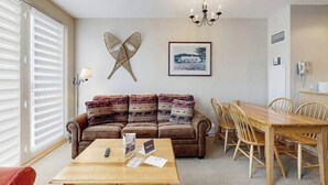 A living room with a sofa, a wooden table, a dining table with chairs, a chandelier, and a framed picture on the wall. - Walk to lifts, condo at Stratton Mountain, fireplace, pool, hot tubs, sauna (Stratton)