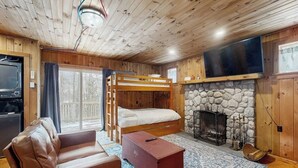 A cozy cabin with a bunk bed, a fireplace, a television, and a leather sofa. - Cozy studio cabin w/ seasonal mountain views, wrap-around deck, window a/c, bbq (Wardsboro)