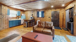 A wooden cabin interior with a kitchenette, a brown leather sofa, and a remote control on a table. - Cozy studio cabin w/ seasonal mountain views, wrap-around deck, window a/c, bbq (Wardsboro)
