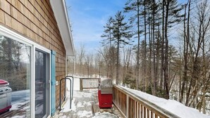 A wooden deck with a glass door leading to a vehicle, surrounded by snow-covered ground and trees. - Cozy studio cabin w/ seasonal mountain views, wrap-around deck, window a/c, bbq (Wardsboro)