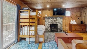 A cabin with a bunk bed, a stone fireplace, a television, and a wooden dresser. - Cozy studio cabin w/ seasonal mountain views, wrap-around deck, window a/c, bbq (Wardsboro)