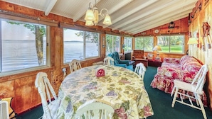 A cabin with a round dining table, wooden walls, and large windows overlooking a body of water. - Dog-Friendly Lakefront Home with WiFi, Private Dock & Firepit (Grand Isle)
