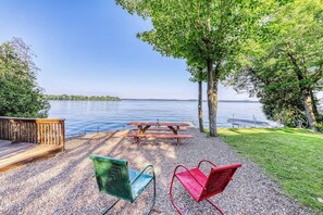 Järvenrantainen piknikalue, jossa on puinen terassi, piknikpöytä ja kaksi metallituolia.