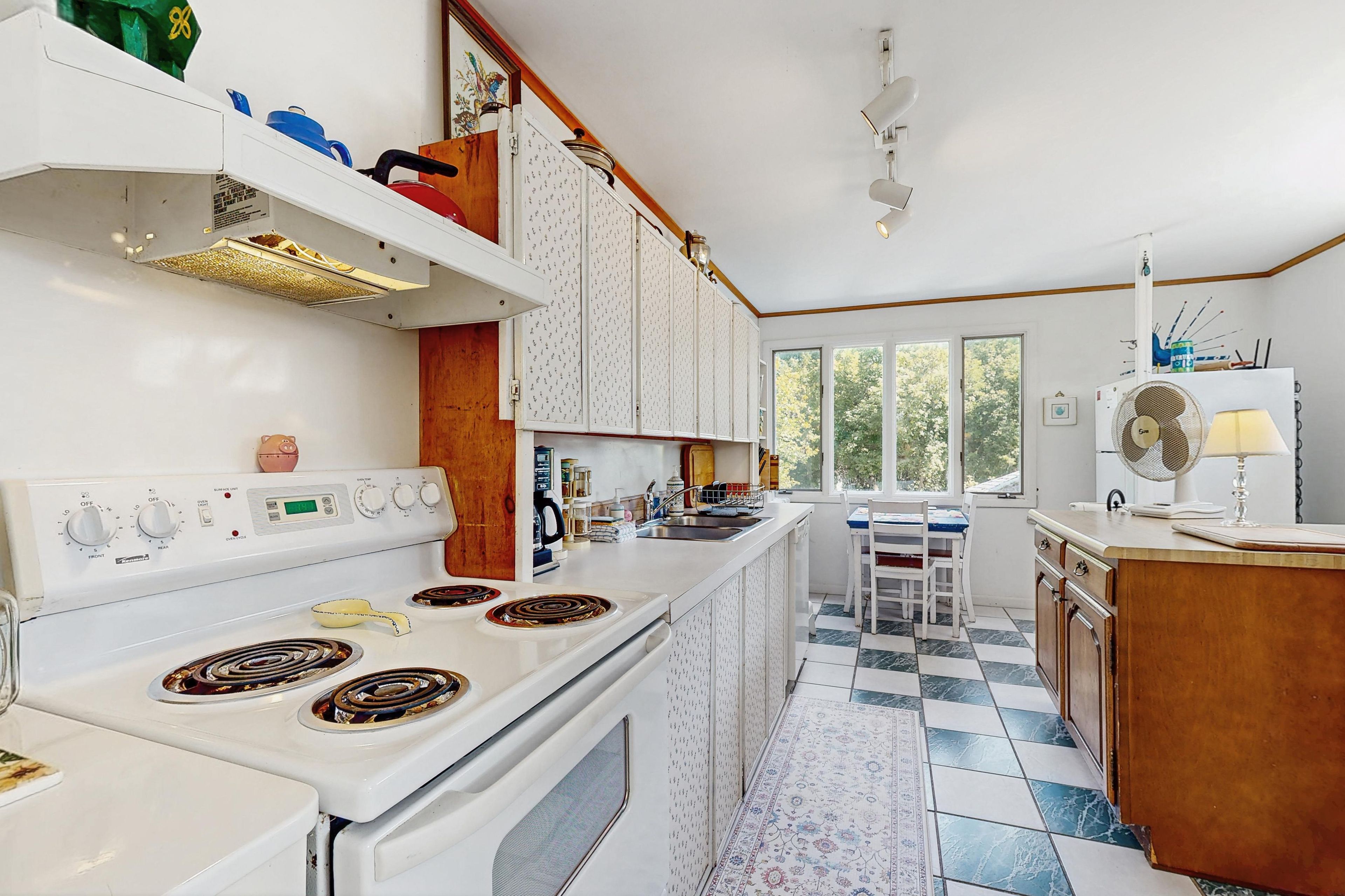 Una cocina con estufa blanca, un lavamanos y un ventanal.