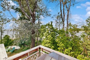 A wooden deck with a metal railing overlooking a body of water, surrounded by trees and greenery.