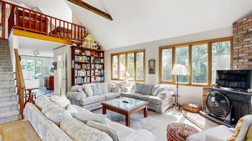 Een ruime woonkamer met een grote hoekbank, een open haard en een boekenkast vol boeken.