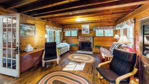 A log cabin interior with a bed, seating area, fireplace, and wooden walls. - Dog-Friendly Lakefront, w/Free WiFi, Patio, Deck/Dock, & Rustic Water Views (Charlotte)