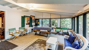 A spacious room with a large window, a wooden bench, a wicker sofa, and a dining table. - Dog-Friendly Lakefront, w/Free WiFi, Patio, Deck/Dock, & Rustic Water Views (Charlotte)