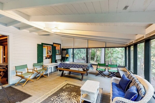 A spacious room with a large window, a wooden bench, a wicker sofa, and a dining table. - Dog-Friendly Lakefront, w/Free WiFi, Patio, Deck/Dock, & Rustic Water Views (Charlotte)