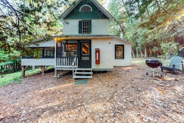 A rustic cabin with a porch, a small deck, and a grill area.