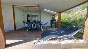 Ein überdachter Außenbereich mit Tisch und Stühlen, Liegestühlen und einer Holzterrasse.
