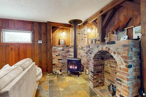 A cozy room with a brick fireplace, a sofa, and a window. - Inviting riverfront home with hot tub on deck & fireplace, near skiing & golf (Montgomery)