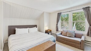 Ett sovrum med en stor säng, en bänk, en soffa, ett fönster med gardiner och en taklampa.