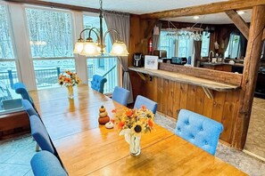 A wooden dining table with chairs, a vase of flowers, and a kitchen area with a wooden counter and hanging lights. - Inviting riverfront home with hot tub on deck & fireplace, near skiing & golf (Montgomery)
