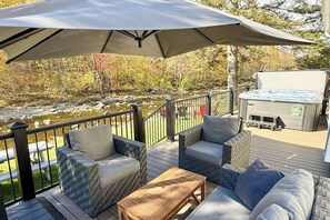 A deck with outdoor furniture, a hot tub, and a view of a river. - Inviting riverfront home with hot tub on deck & fireplace, near skiing & golf (Montgomery)